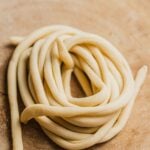 Nest of pici pasta on a wooden surface.