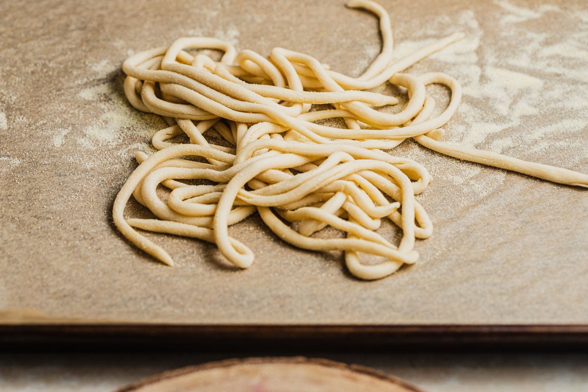 Strands of pici on a semolina-dusted baking sheet.