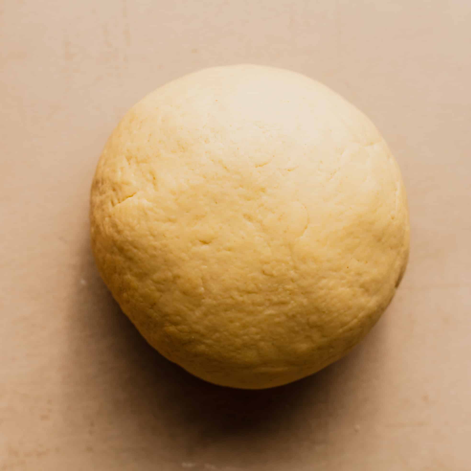A smooth ball of semolina pasta dough on a countertop.