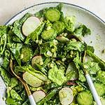 A bowl of salad with butter lettuce, cucumbers, and radish tossed in a creamy dressing with two spoons in it.