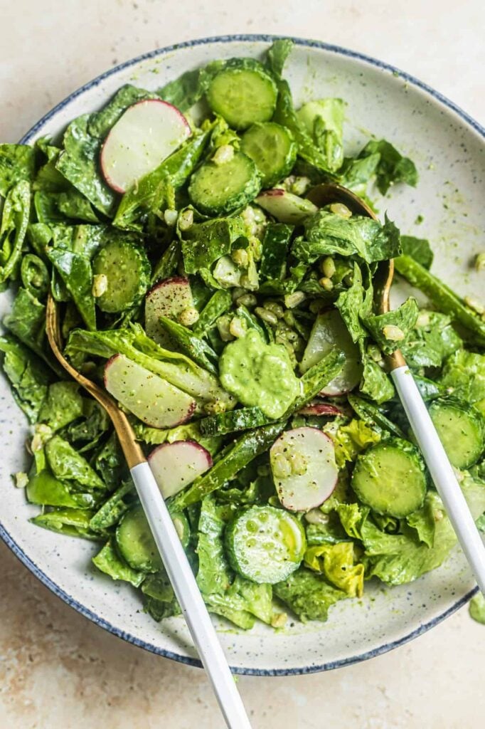 A bowl of salad with butter lettuce, cucumbers, and radish tossed in a creamy dressing with two spoons in it.