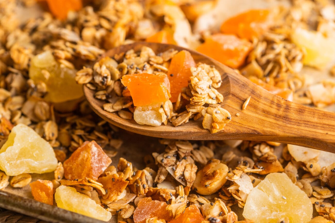 A wooden spoon resting on top of granola with tropical fruit.
