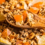 A wooden spoon resting on top of granola with tropical fruit.