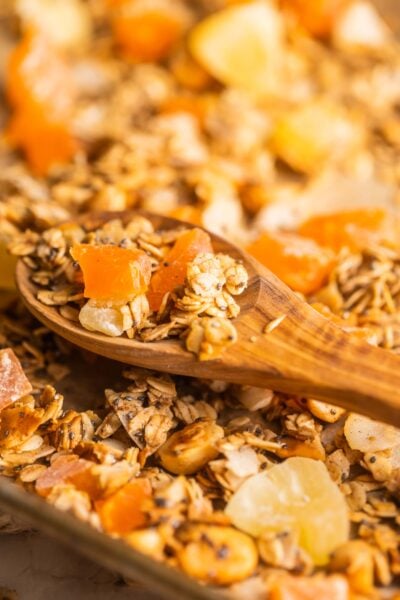 A wooden spoon scooping granola off a baking sheet