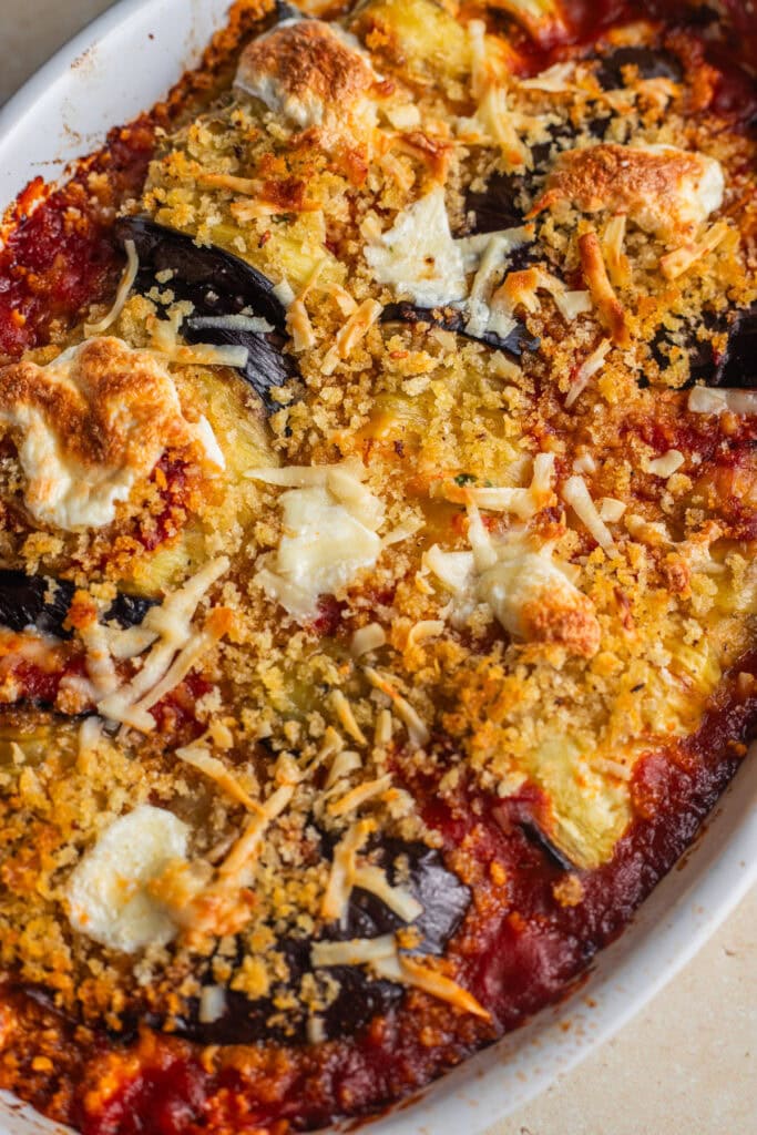 A casserole dish with eggplant involtini in tomato sauce topped with breadcrumbs and cheese.
