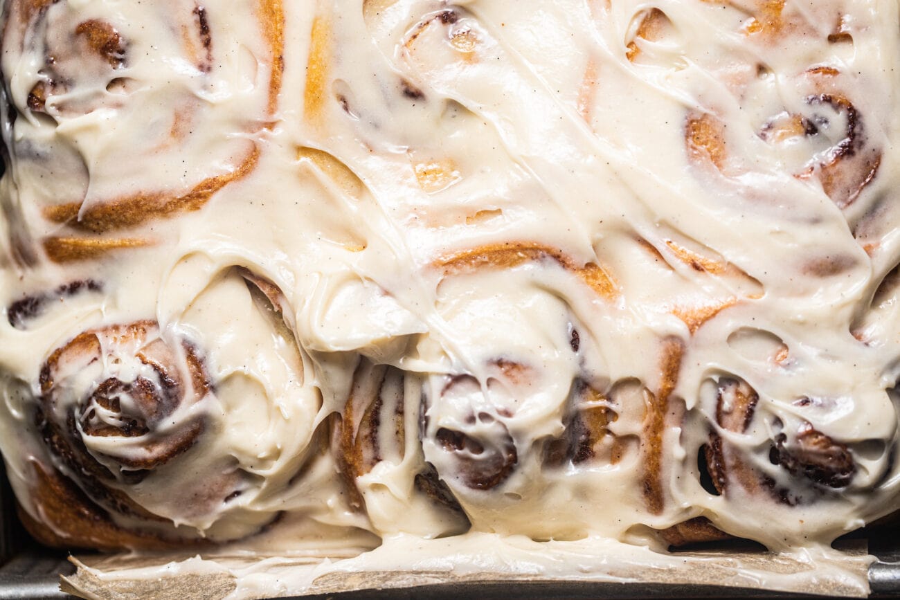 Cream cheese icing with specks of vanilla bean frosted on top of cinnamon rolls.
