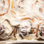 Cream cheese icing with specks of vanilla bean frosted on top of cinnamon rolls.