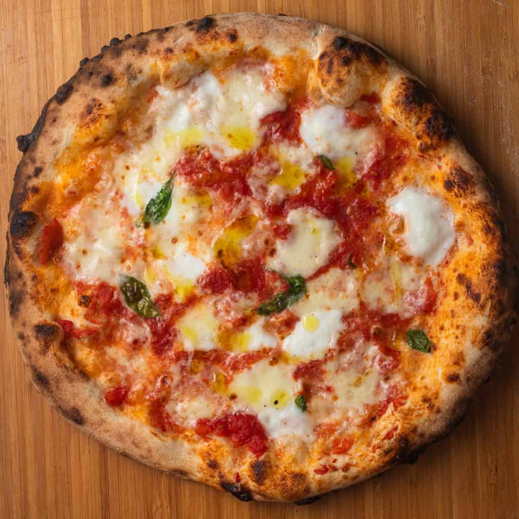 A margherita pizza with a charred crust on a wooden pizza peel.