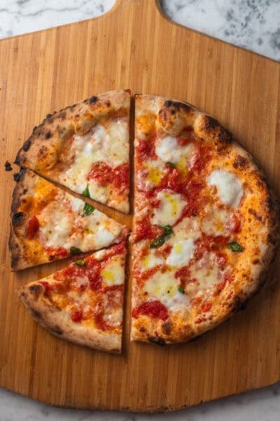 A margherita pizza with a charred crust sliced into a few slices on a pizza peel set on a countertop.