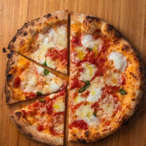 A margherita pizza with a charred crust sliced into a few slices on a pizza peel set on a countertop.