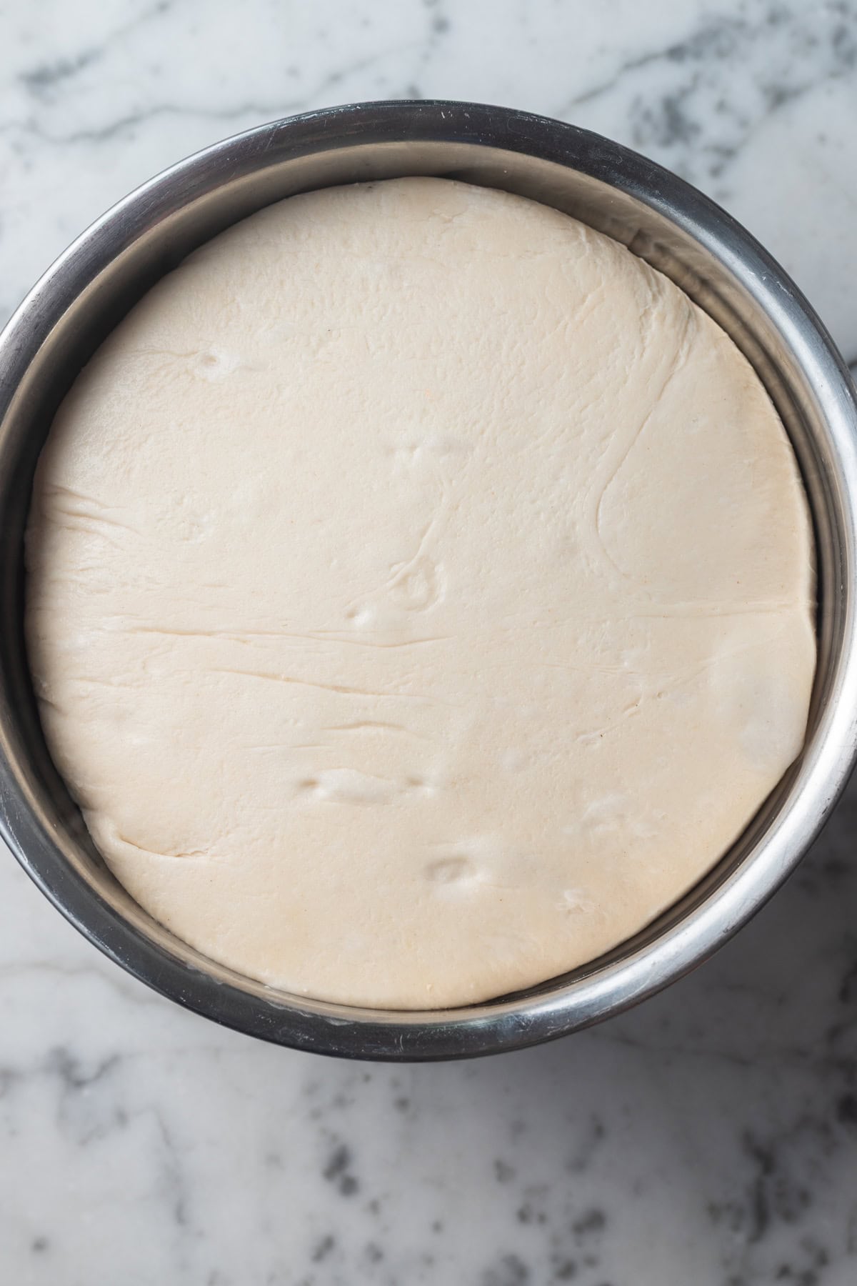 Dough rising in a metal mixing bowl with visible gas bubbles.