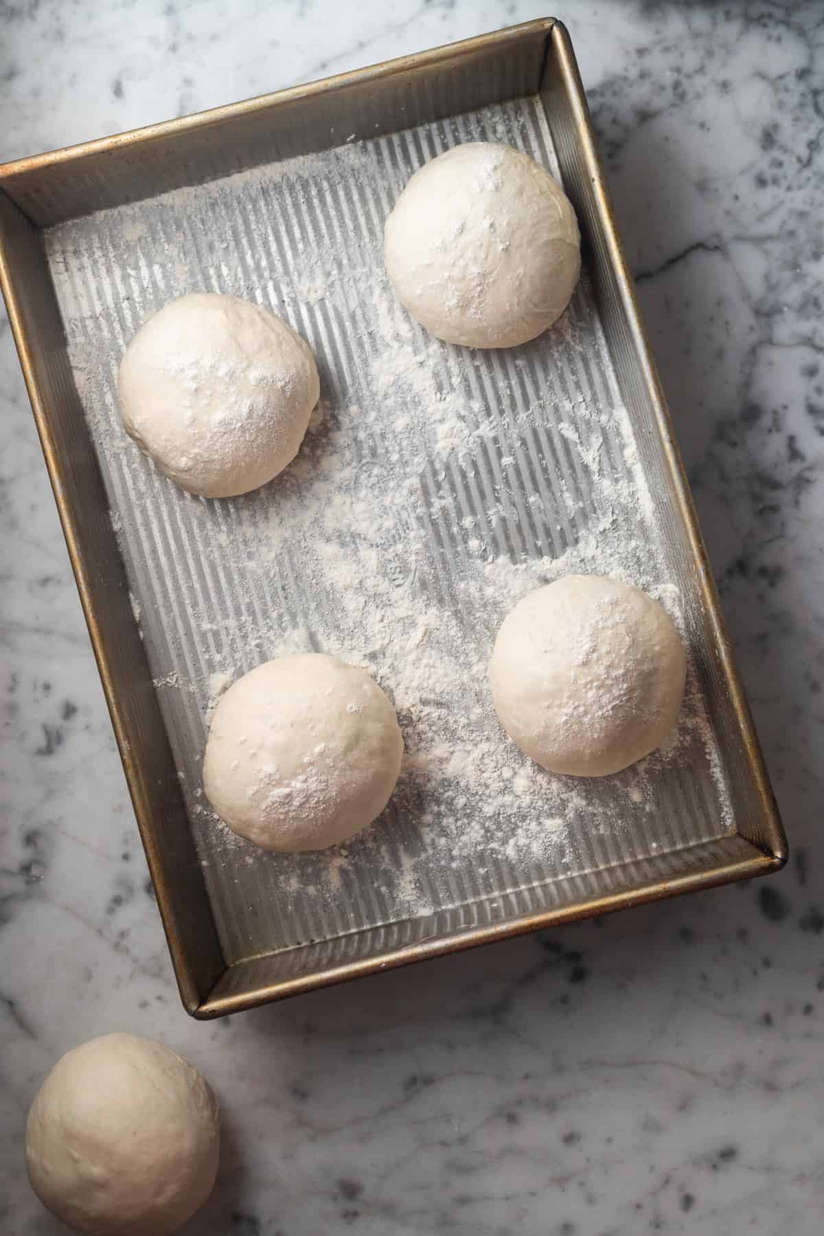 Dough balls dusted with flour in a metal baking pan.