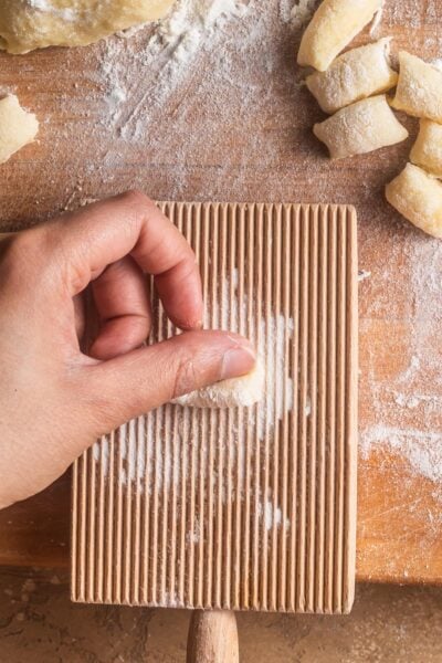 Hand rolling a piece of gnocchi dough over a gnocchi board on a cutting board.