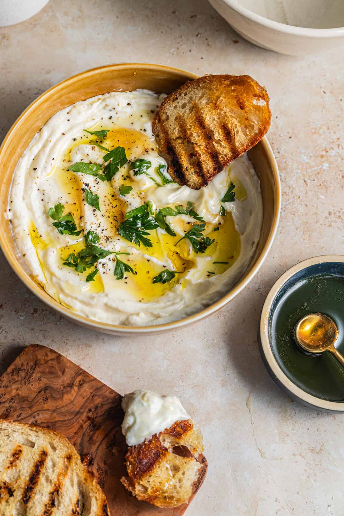 Grilled bread in a bowl of whipped ricotta with more bread on a cutting board in the background.