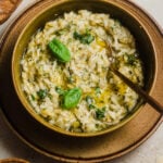Bowl of risotto with herbs on top and cheese in the background