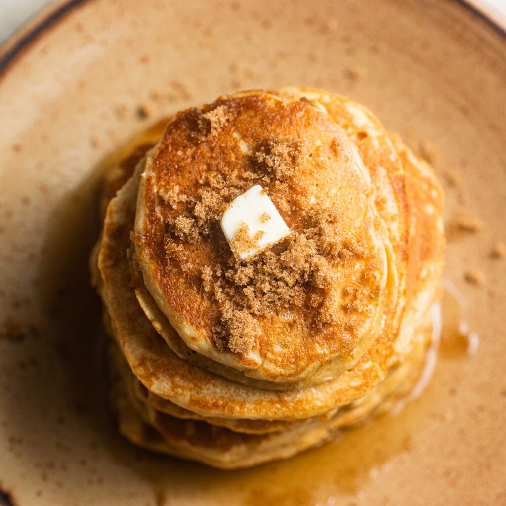 Stack of pancakes with brown sugar and a pat of butter on top on a plate.