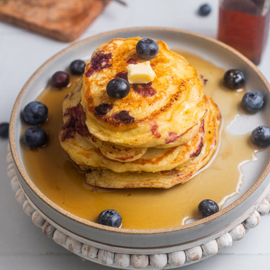 Stack of lemon blueberry pancakes with maple syrup and a pat of butter.