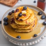 Stack of lemon blueberry pancakes with maple syrup and a pat of butter.