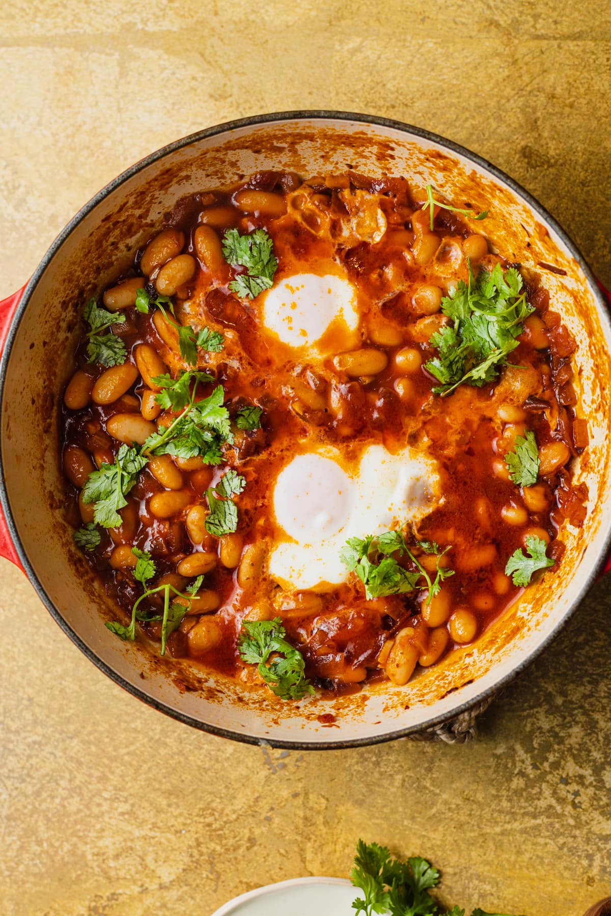 A skillet with poached eggs and beans in tomato sauce topped with cilantro.