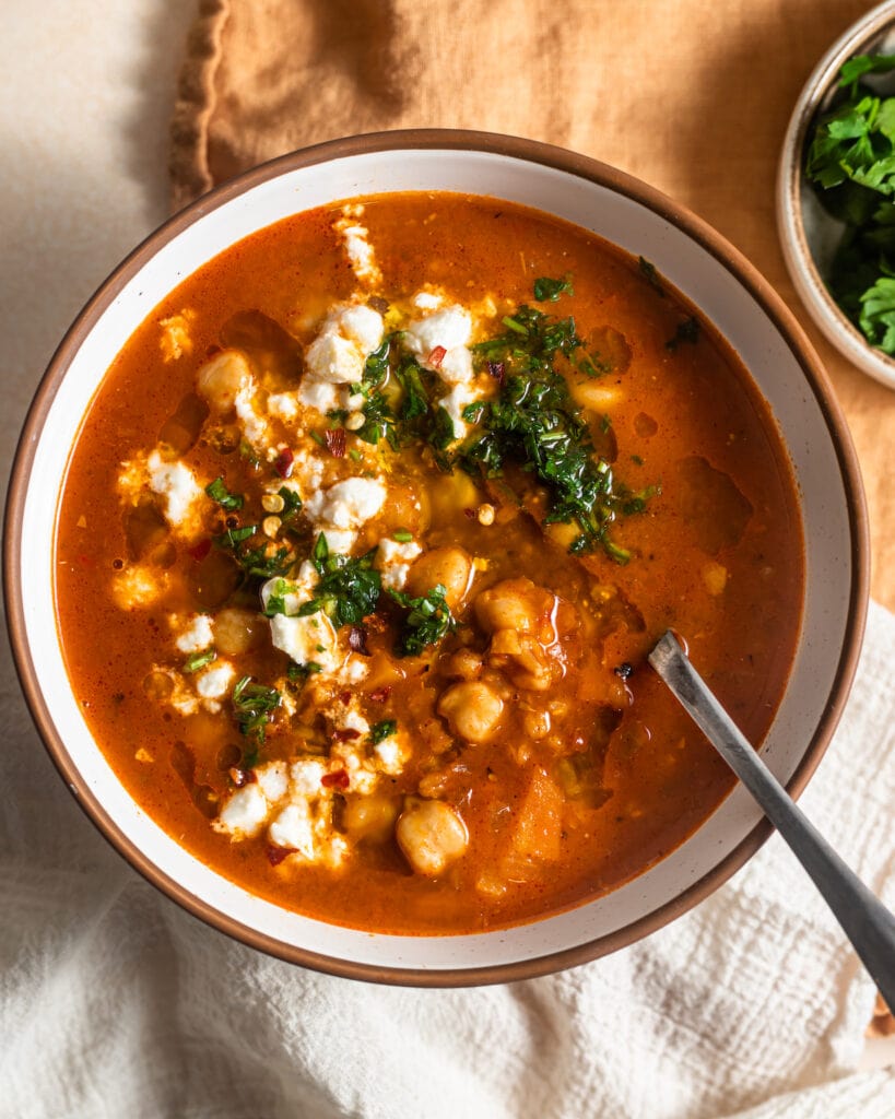 Bowl of chickpea soup topped with herbs and feta cheese.