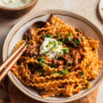 Bowl of lamb ragu and mafaldine pasta with a bowl of ricotta in the background.