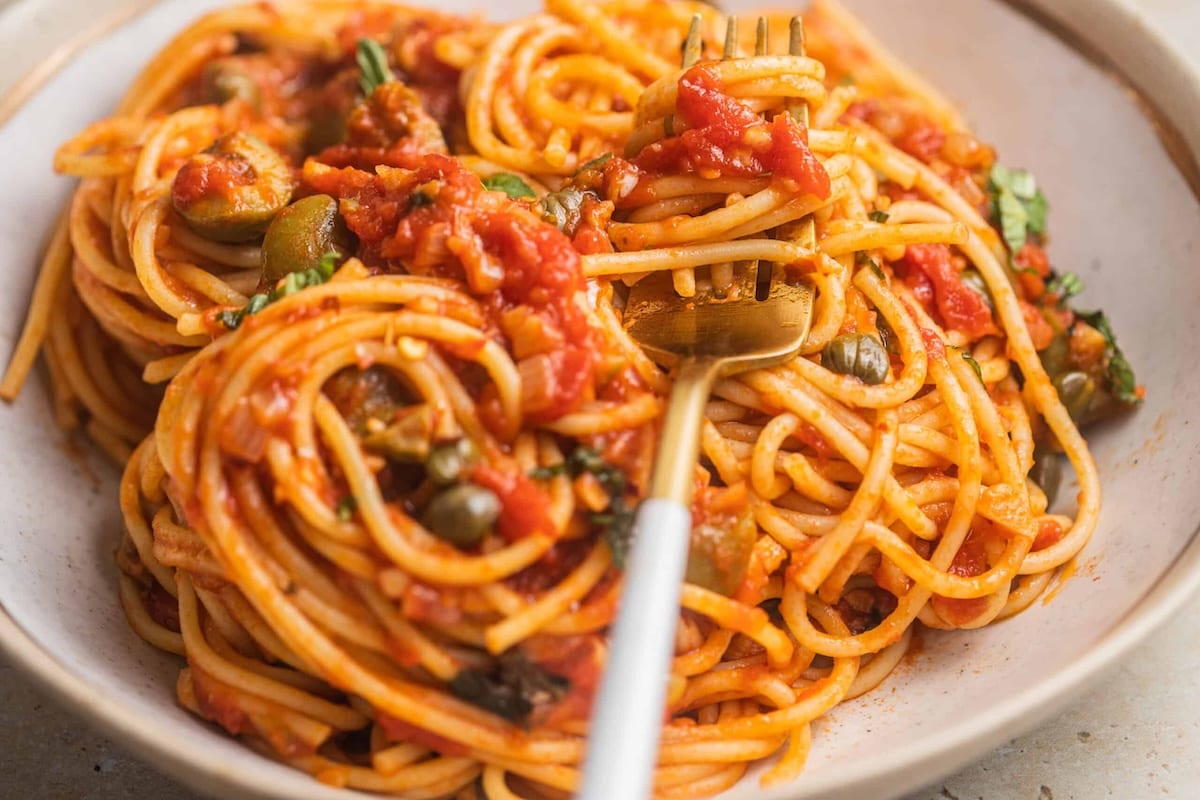A bowl of spaghetti arrabbiata with capers and olives in a bowl with a fork.