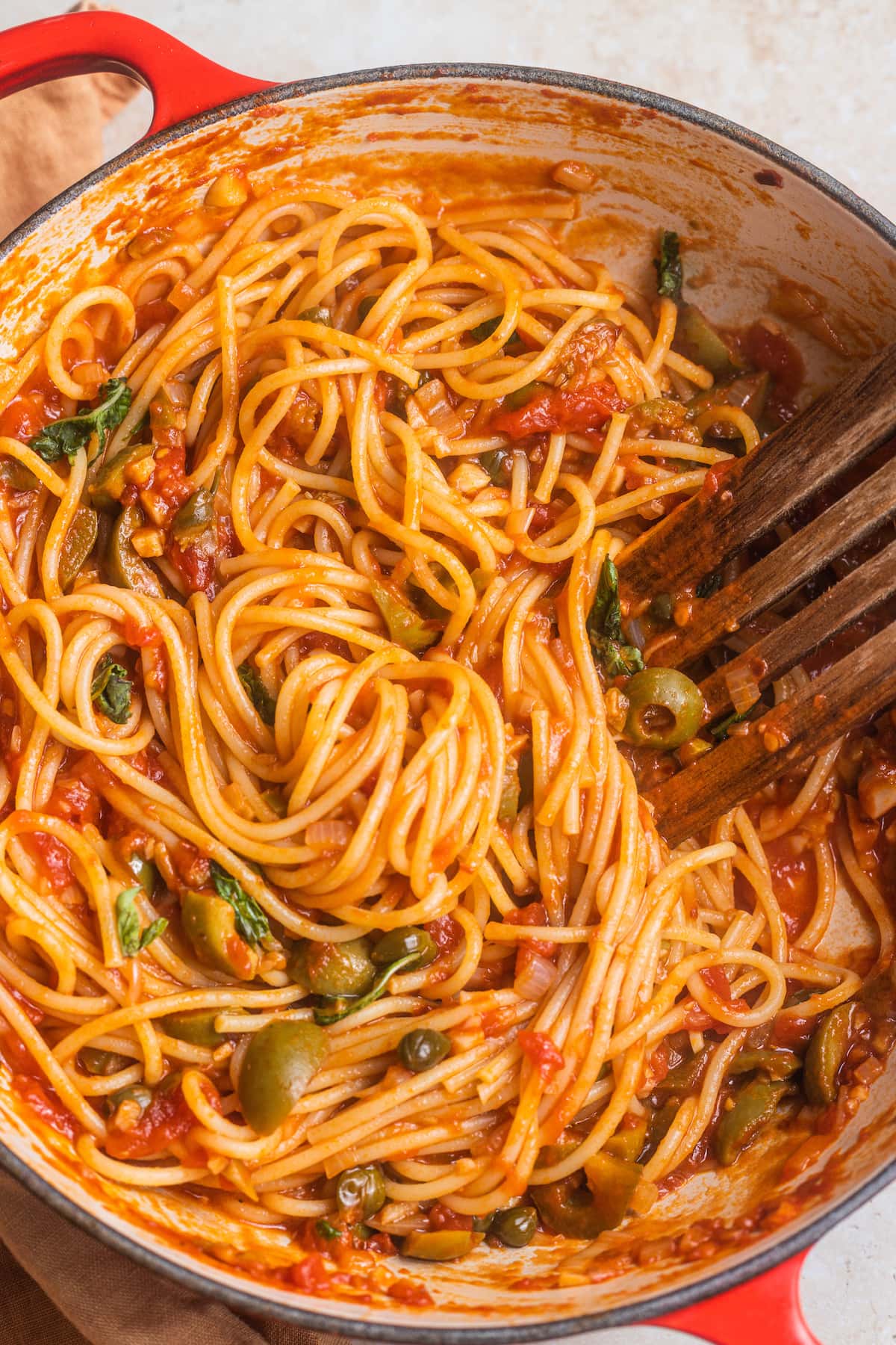 Spaghetti tossed in arrabbiata sauce with a wooden spatula in a skillet.