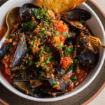 Bowl of mussels tossed in marinara sauce garnished with herb breadcrumbs.