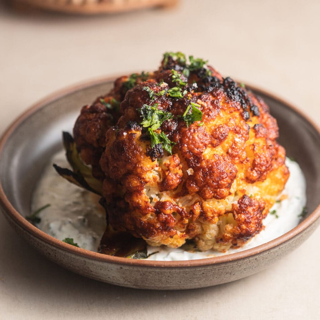 Whole-roasted harissa cauliflower set atop a bowl of yogurt.