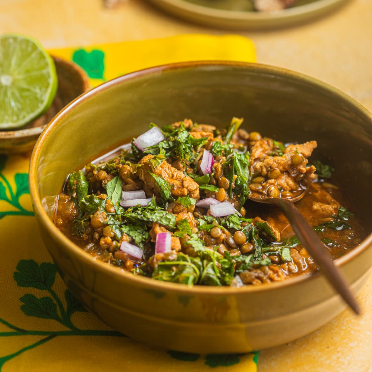 A bowl filled with turkey lentil soup with a lime in the background.