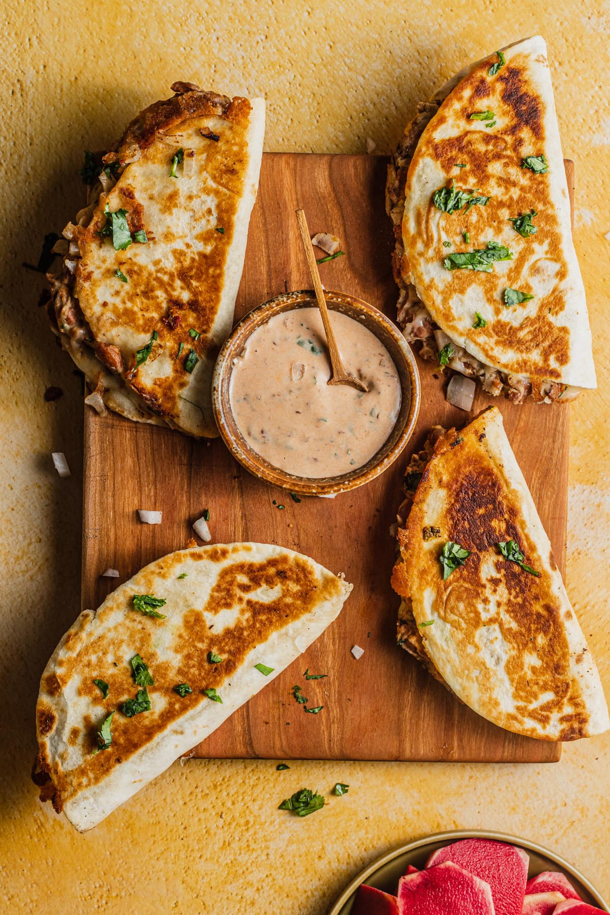 4 tacos filled with bean and cheese arranged on a wooden cutting board with a bowl of creamy chipotle sauce in the background.
