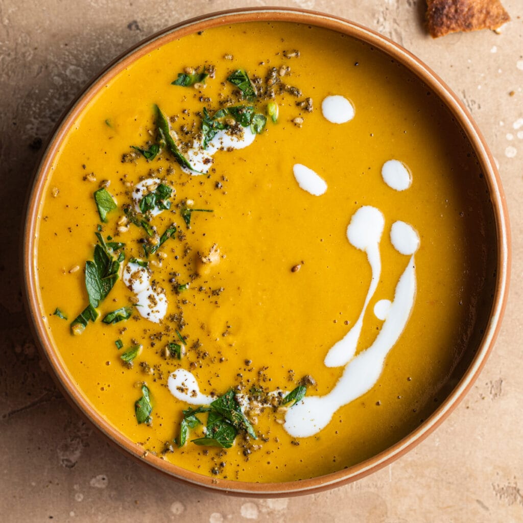 A bowl of soup decorated with a ring of yogurt sauce, herbs, and zaatar spices.