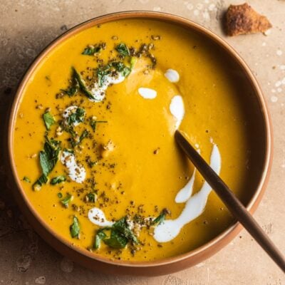 Bowl of carrot soup topped with a swirl of yogurt and herbs.