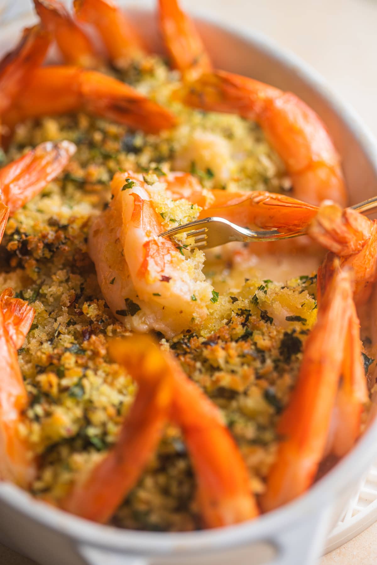 Small golden fork piercing a cooked shrimp surrounded by breadcrumbs and shrimp tails.