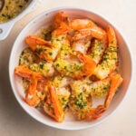 Bowl of cooked shrimp topped with herb breadcrumbs and a casserole in the background.