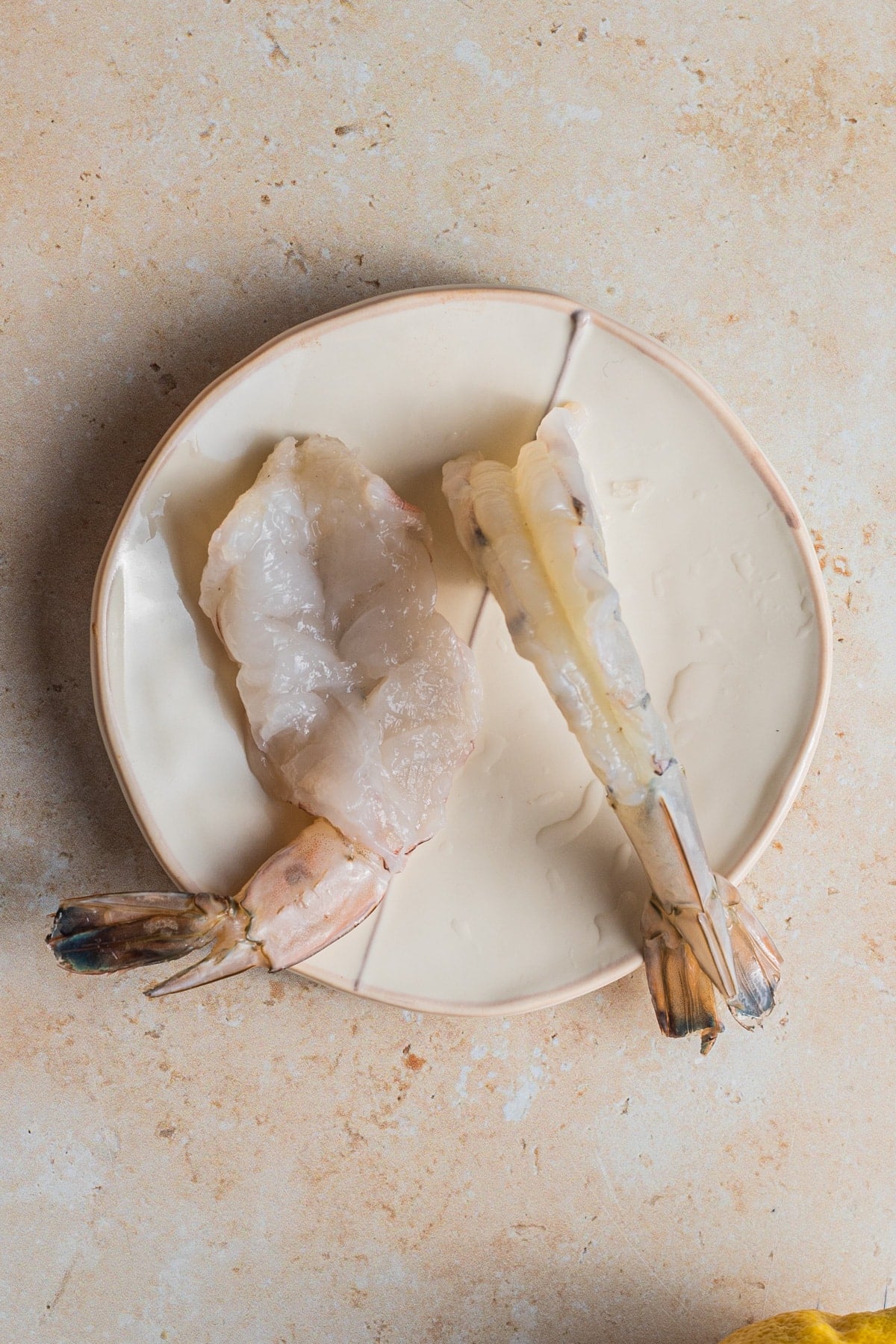 Butterflied shrimp on a small plate set on a tile countertop.