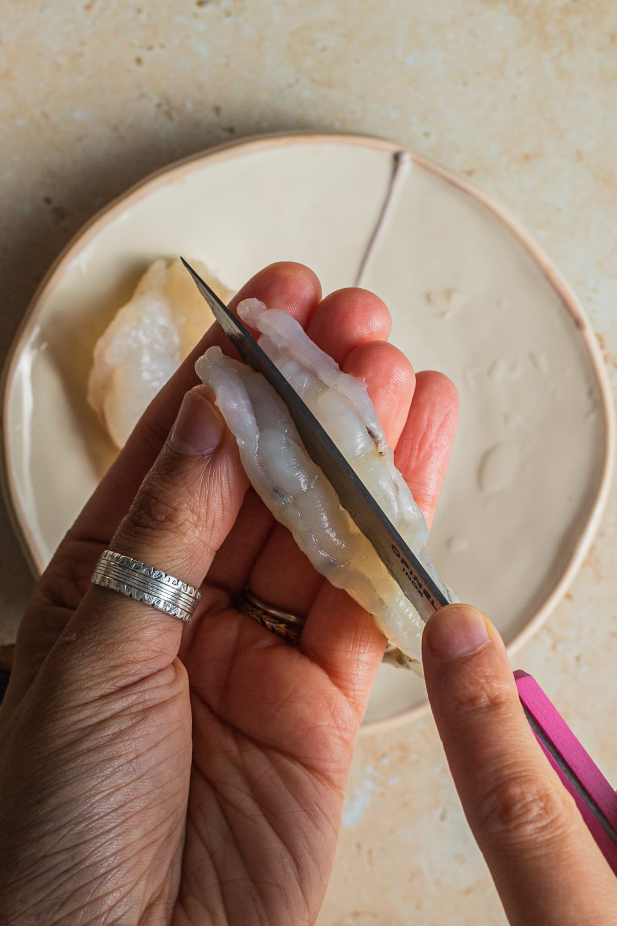 Knife butterflying shrimp over a plate of shrimp. 