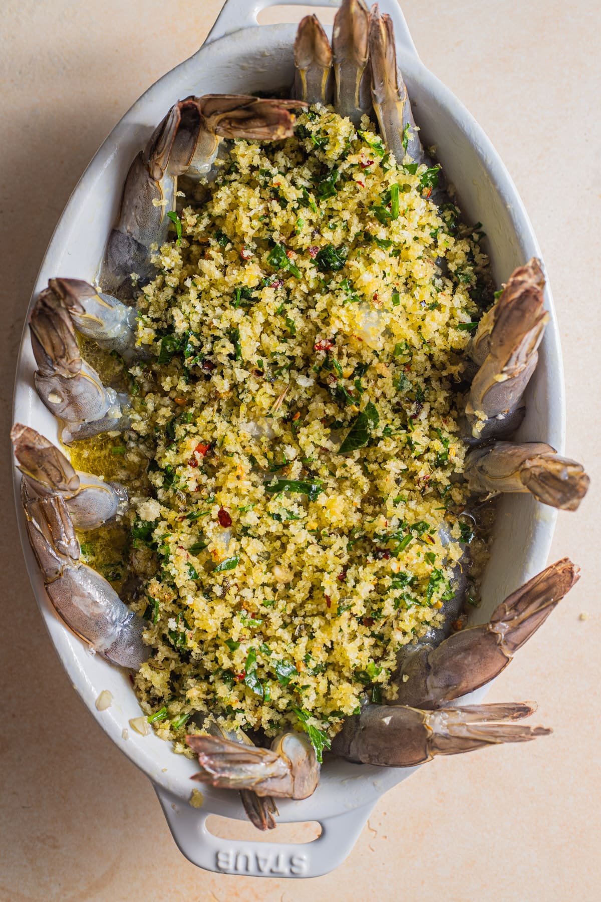 Shrimp tails peeking out of an oval casserole topped with herb breadcrumbs.