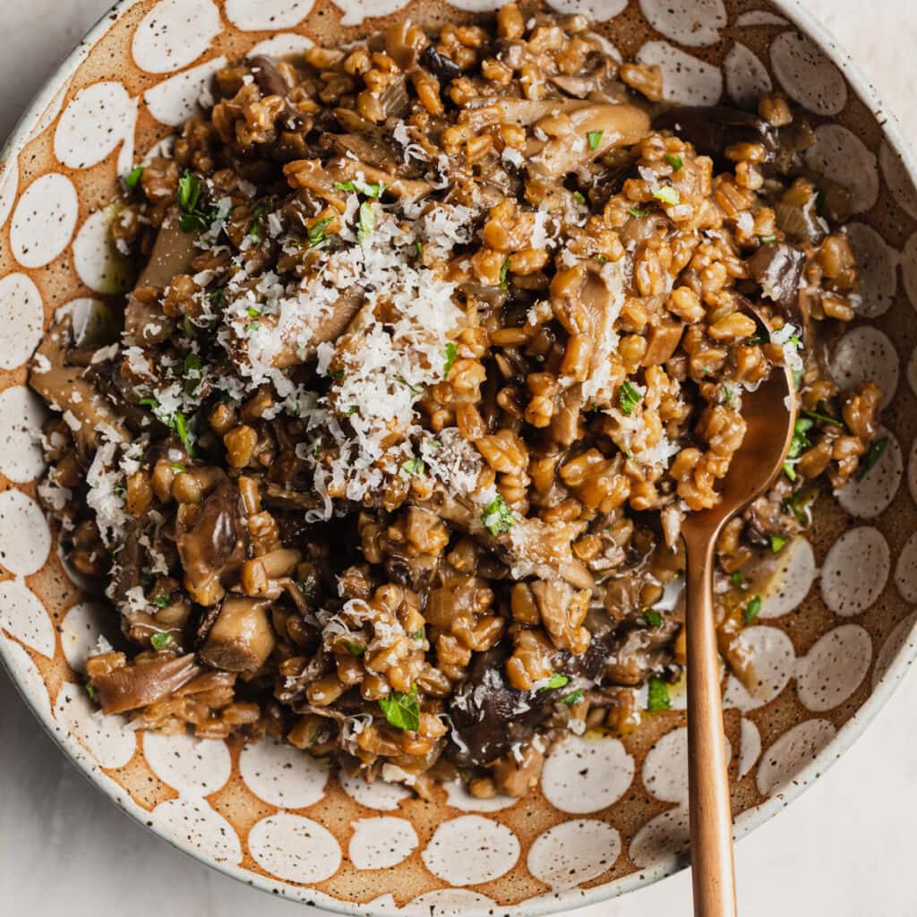 A ceramic spotted bowl with farro risotto, mushrooms, parmesan cheese, and herbs on top.