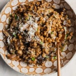 A ceramic spotted bowl with farro risotto, mushrooms, parmesan cheese, and herbs on top.