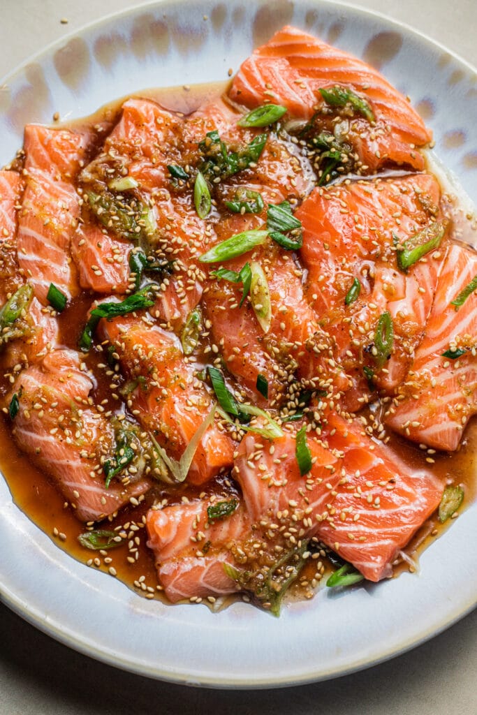 Plate of salmon crudo with a soy-citrus dressing topped with scallions and sesame seeds.
