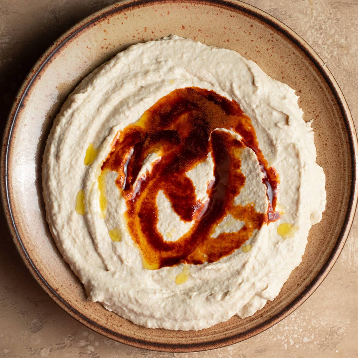 A ceramic plate dolloped with butter bean hummus and a drizzle of paprika oil.