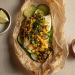 Halibut wrapped in parchment paper topped with corn, olives, and herbs.
