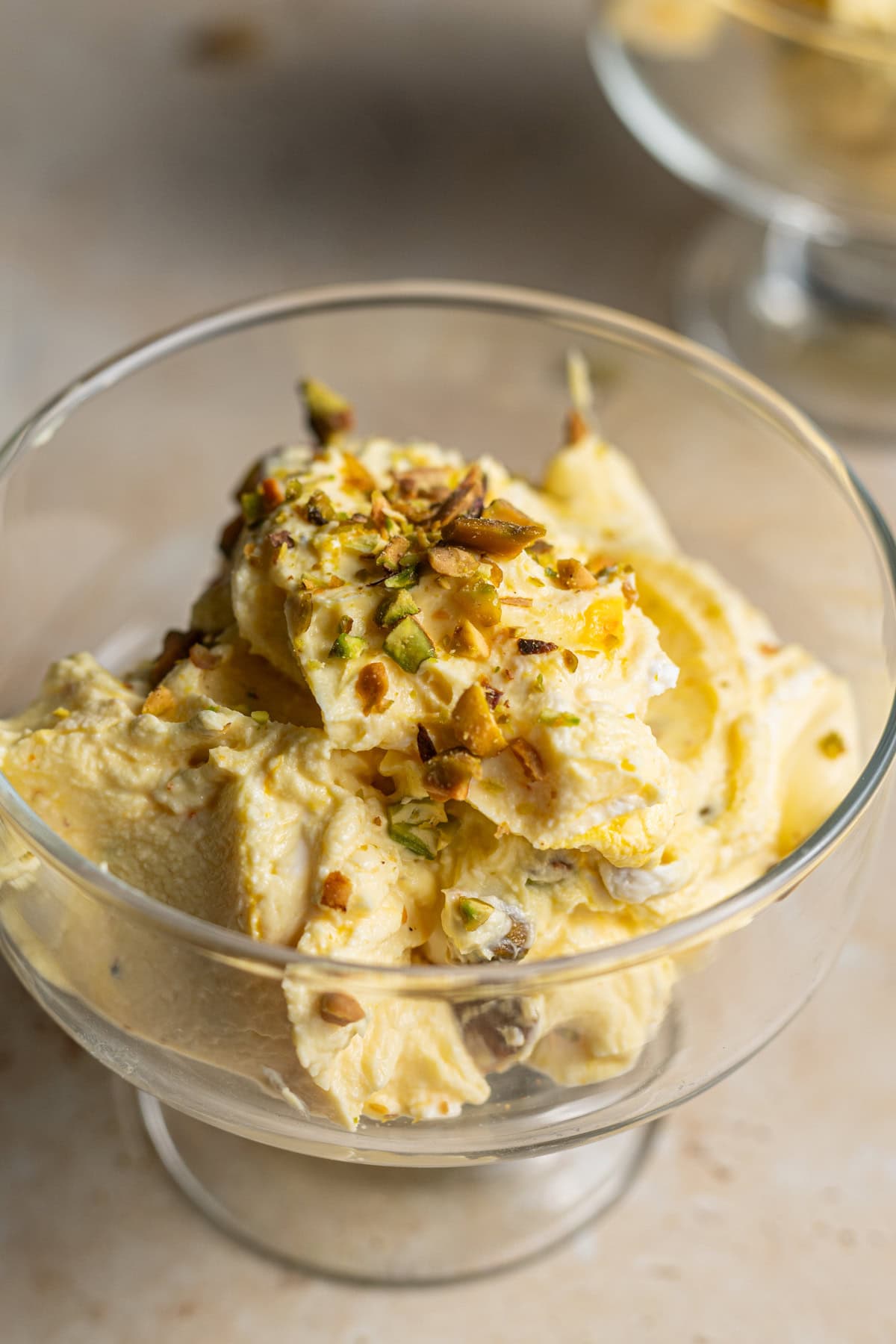 A dessert glass filled with shrikhand topped with chopped pistachios and saffron threads.