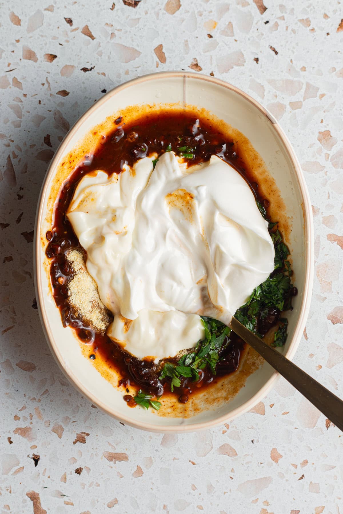 A small bowl with mayonnaise, sour cream, chipotle sauce, garlic powder, and fresh herbs.