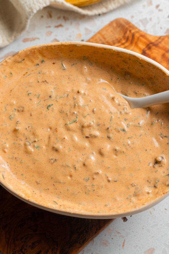 A bowl of creamy chipotle sauce on a small wooden cutting board set on a counter.