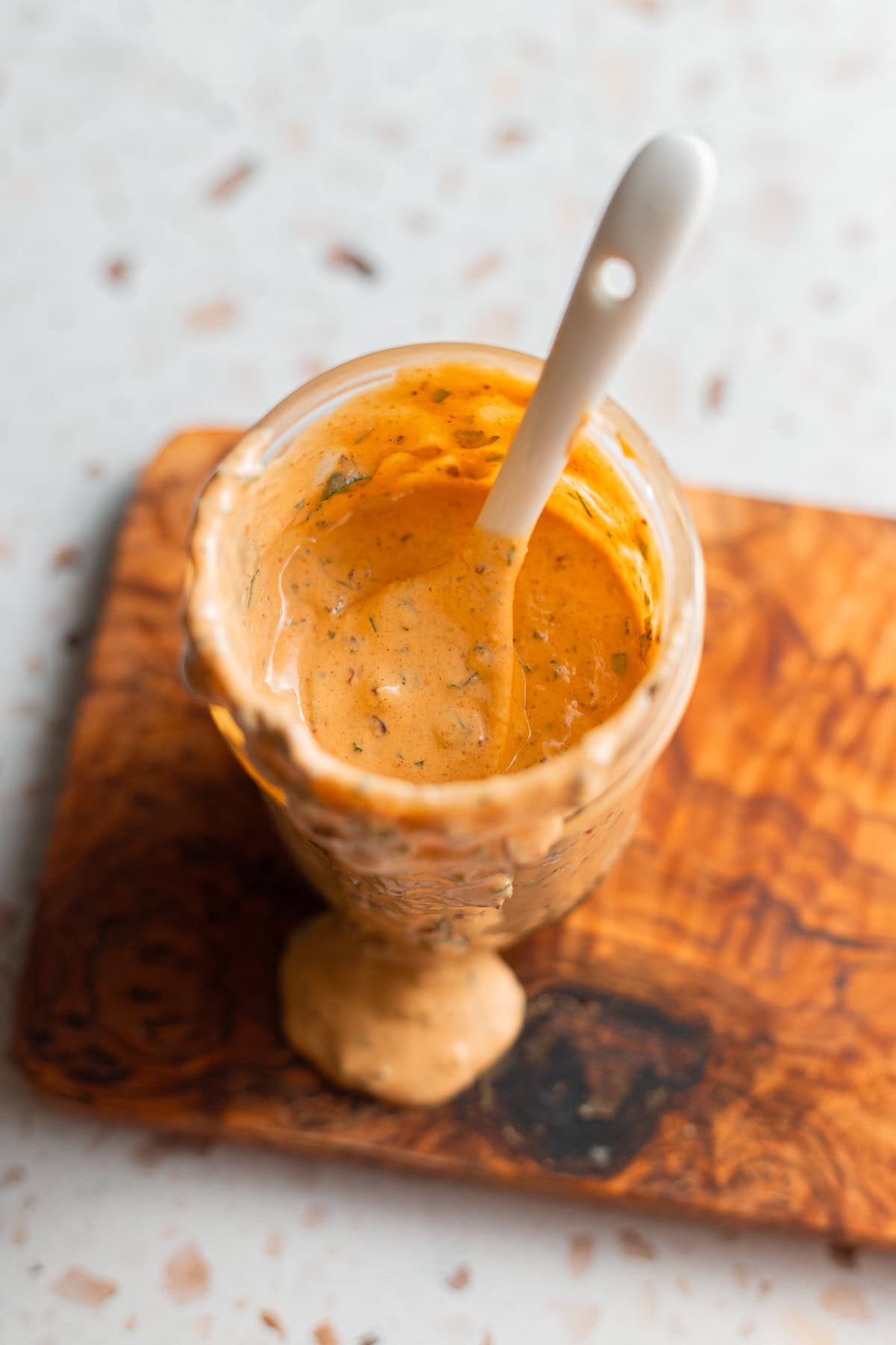 A jar of creamy chipotle sauce with a spoon in it and sauce spilling over onto a cutting board.