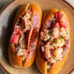 Two lobster rolls on a plate topped with chives and lobster claw meat.