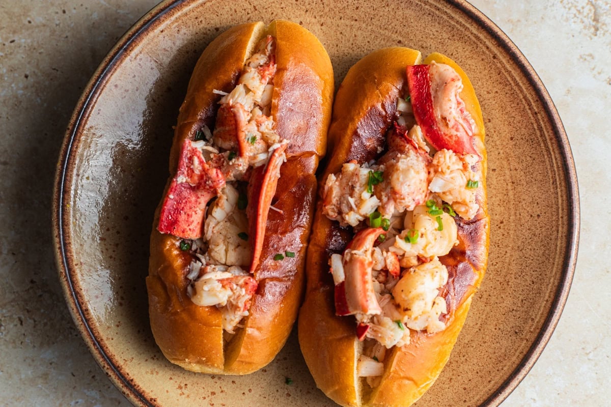 Two lobster rolls on a plate topped with chives and lobster claw meat.