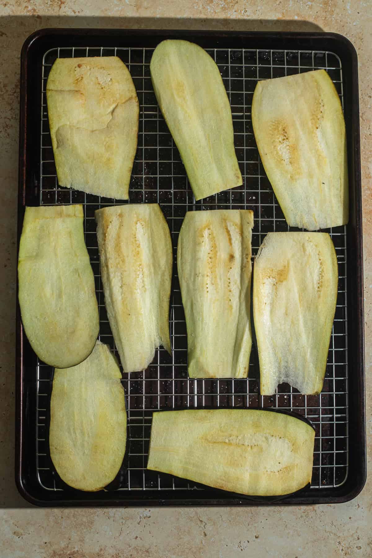 Eggplant slices on a wire cooling rack set over a cutting board.